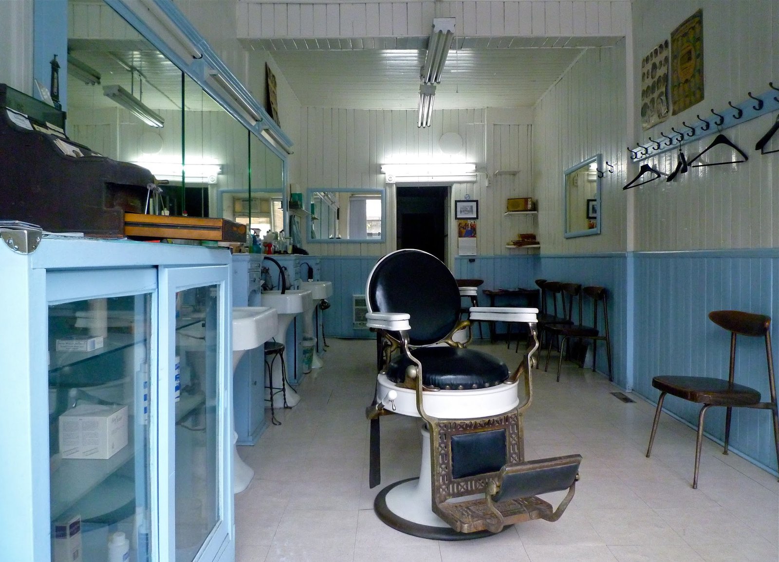 Intérieur vintage de Coiffure Mile-End : chaise de barbier d'époque, lavabos sur pied, miroirs et boiseries bleues.